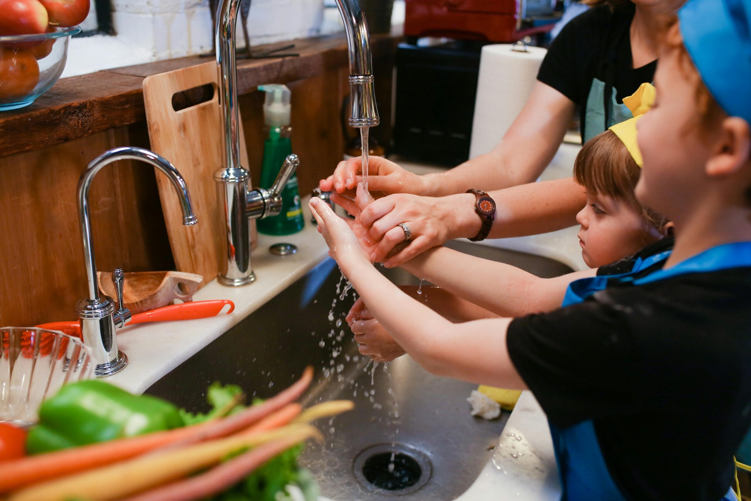 A family cooking activity emphasizing hygiene with kids washing hands in the kitchen.