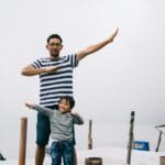 Father and son posing playfully on a wooden dock by the water, enjoying a day outdoors.