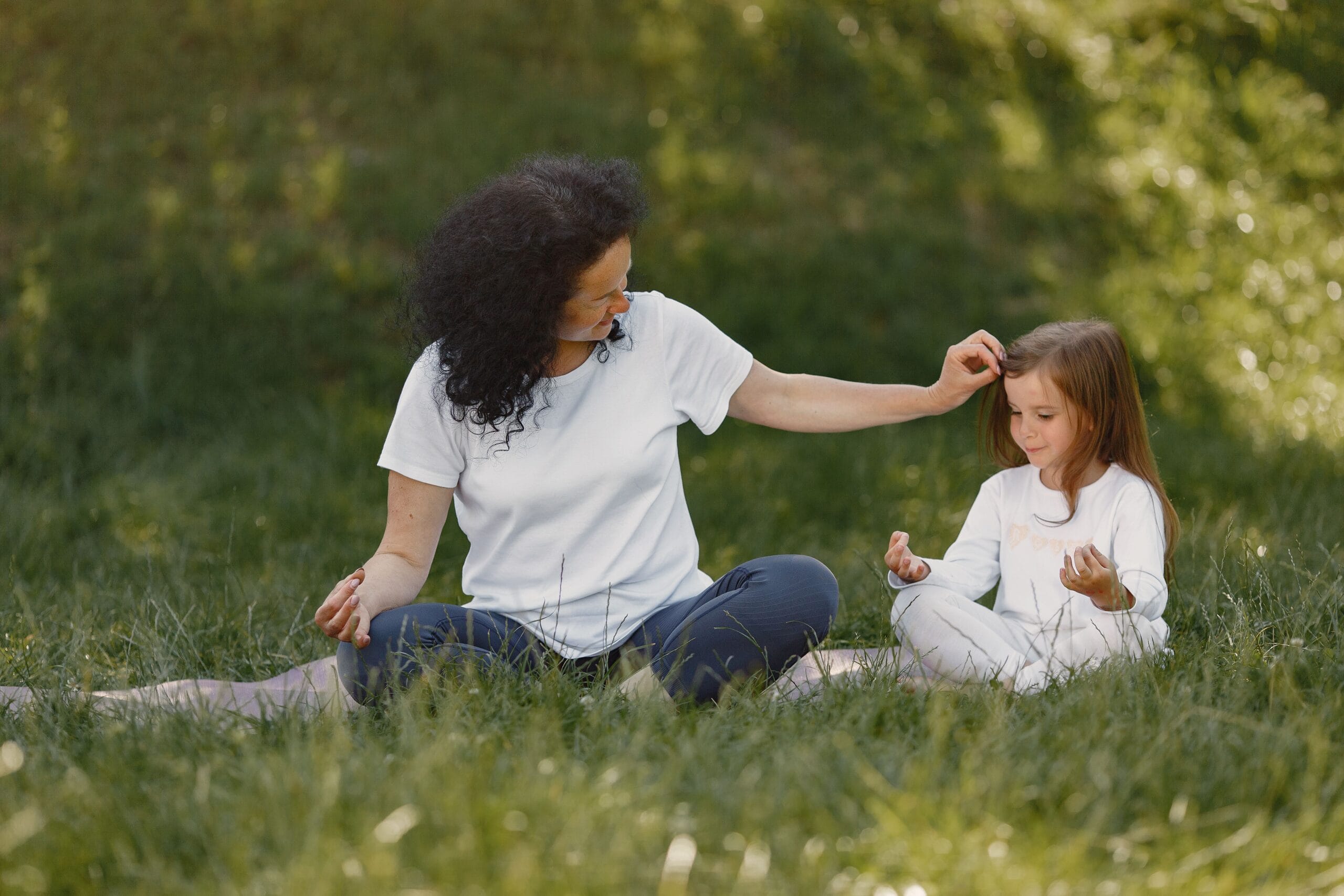 Mother and daughter bonding through yoga outdoors in a serene grassy field.
