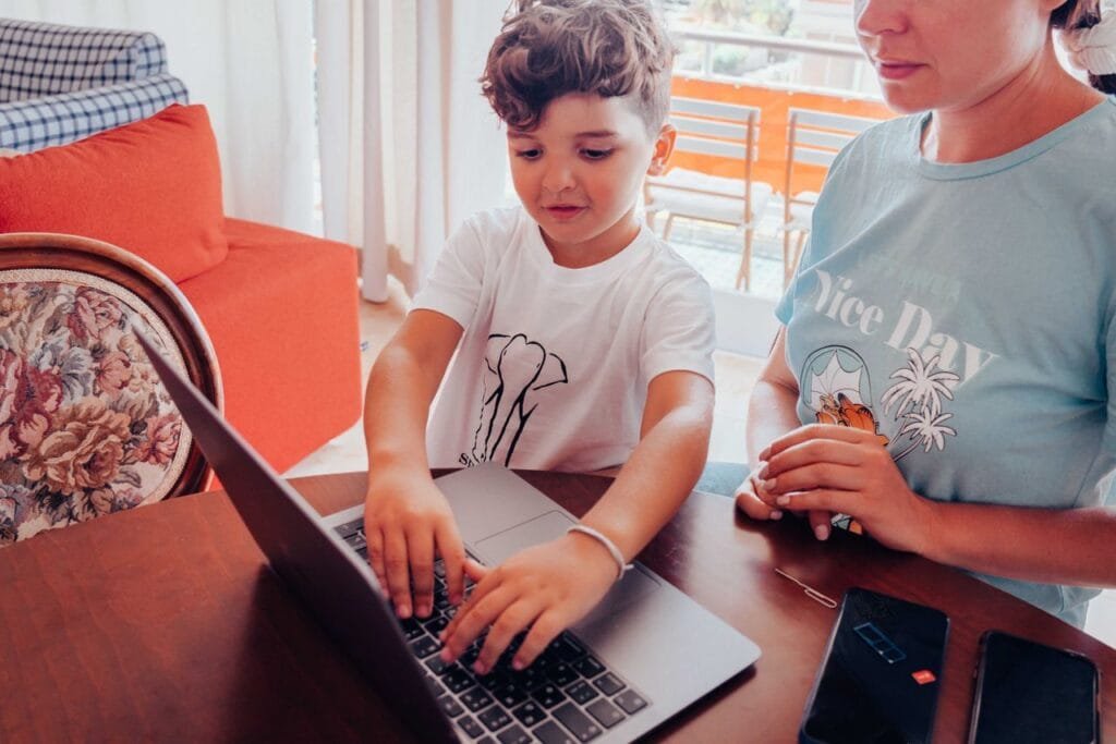 A child and mother engaging with a laptop at a home table, focused on learning or work.