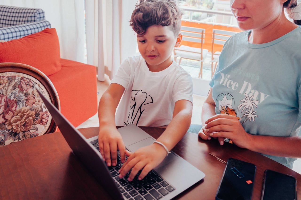 A child and mother engaging with a laptop at a home table, focused on learning or work.