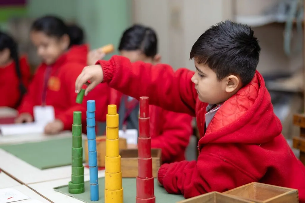 Boy in red jacket stacking colorful blocks in a creative classroom setting.