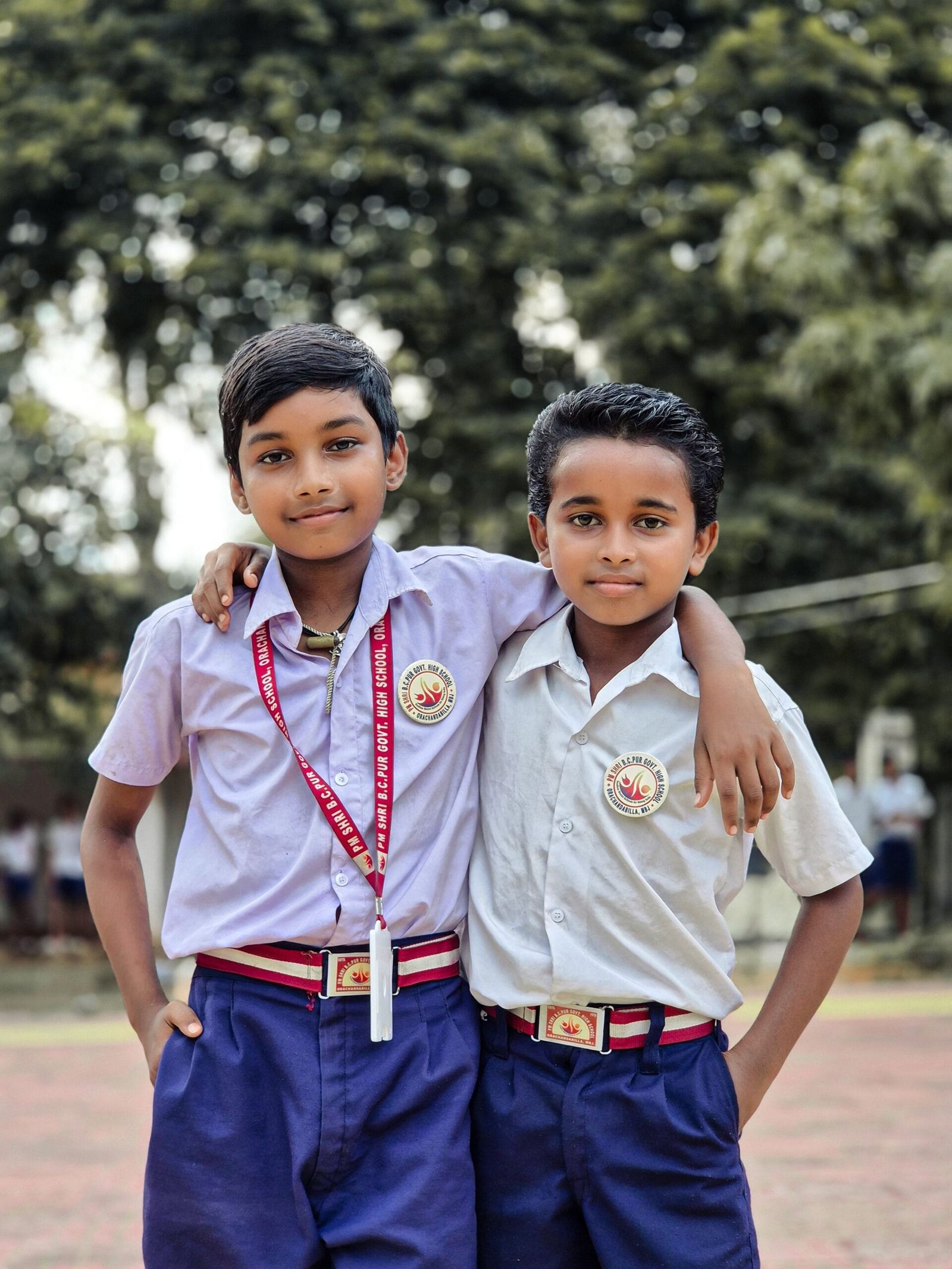 Two young boys in school uniforms smiling outdoors in Baripada, India.
